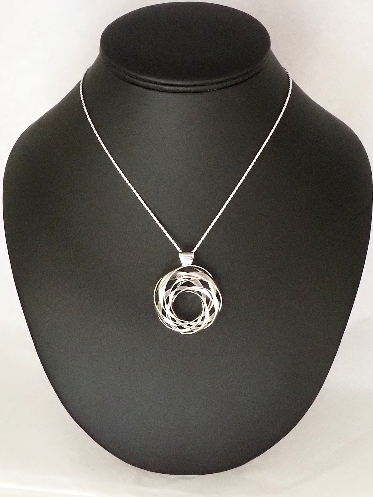 A 35mm rhodium-plated brass cyclide pendant with a silver French rope chain on a necklace display.
