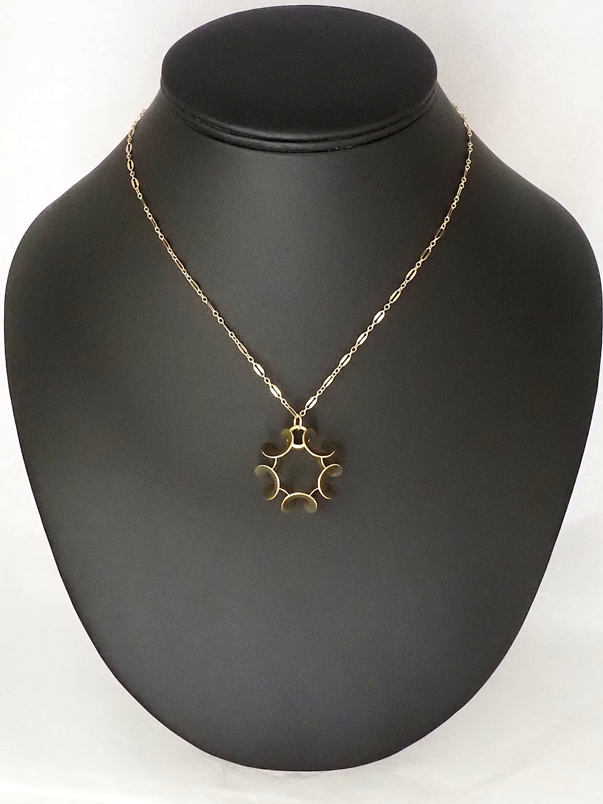 A gold-plated brass pendant in an abstract ruffled shape with five-fold rotational symmetry, with a gold-filled loop chain, on a necklace display.