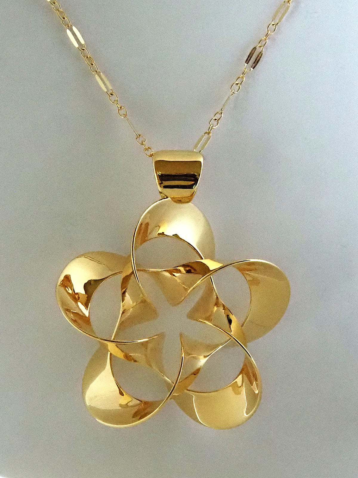 A shiny, gold-plated brass pendant in a flower-like shape with five petals, on a white background.