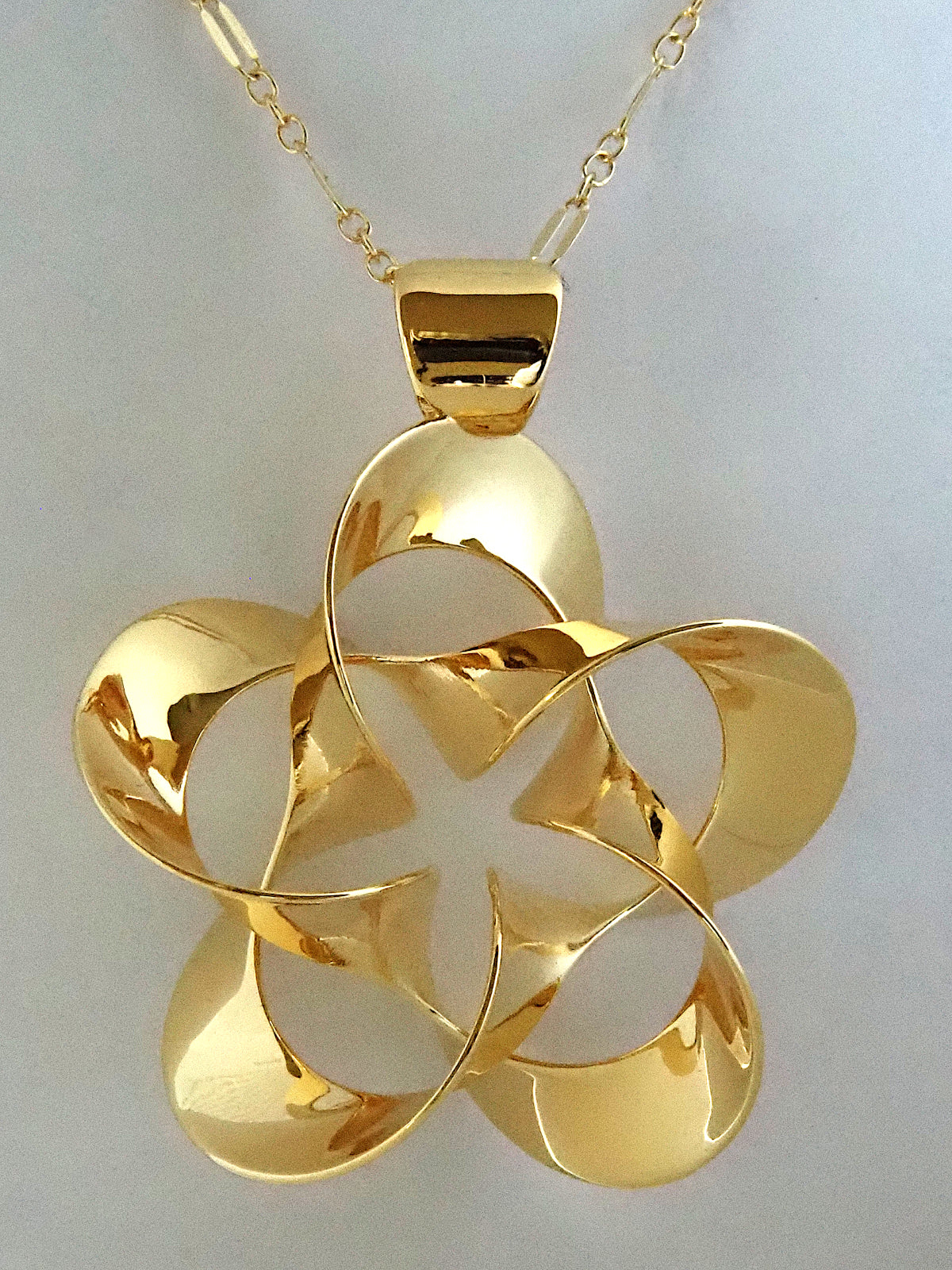 A shiny, gold-plated brass pendant in a flower-like shape with five petals, on a white background.