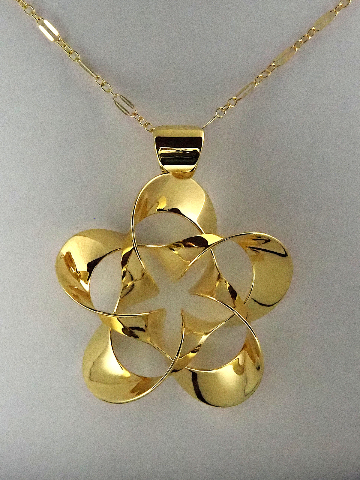 A shiny, gold-plated brass pendant in a flower-like shape with five petals, on a white background.