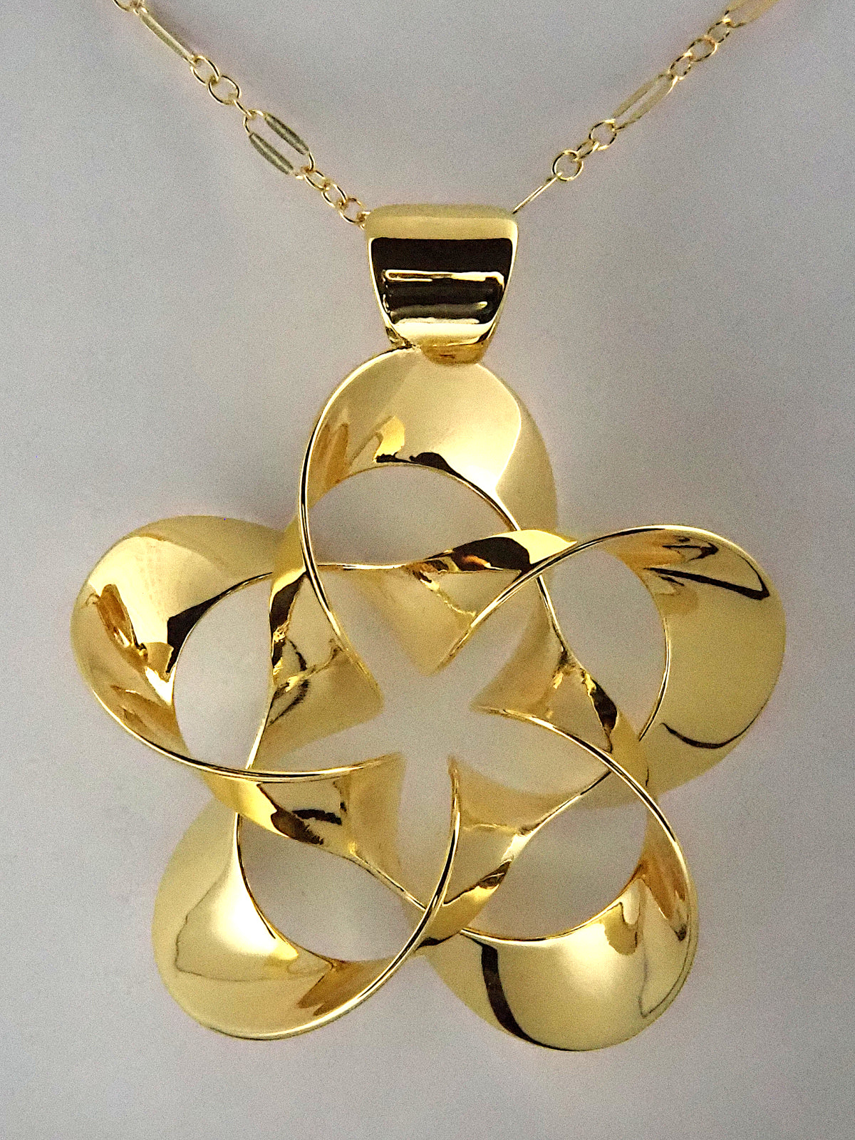 A shiny, gold-plated brass pendant in a flower-like shape with five petals, on a white background.