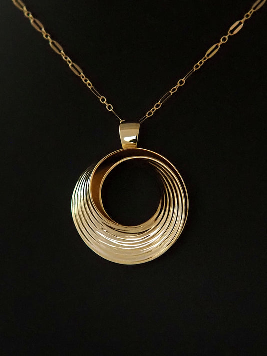 Photograph of a round, gold-plated silver pendant in the shape of a Moebius strip split into two layers, and ridged on the outside, on a gold long-and-short loop chain.