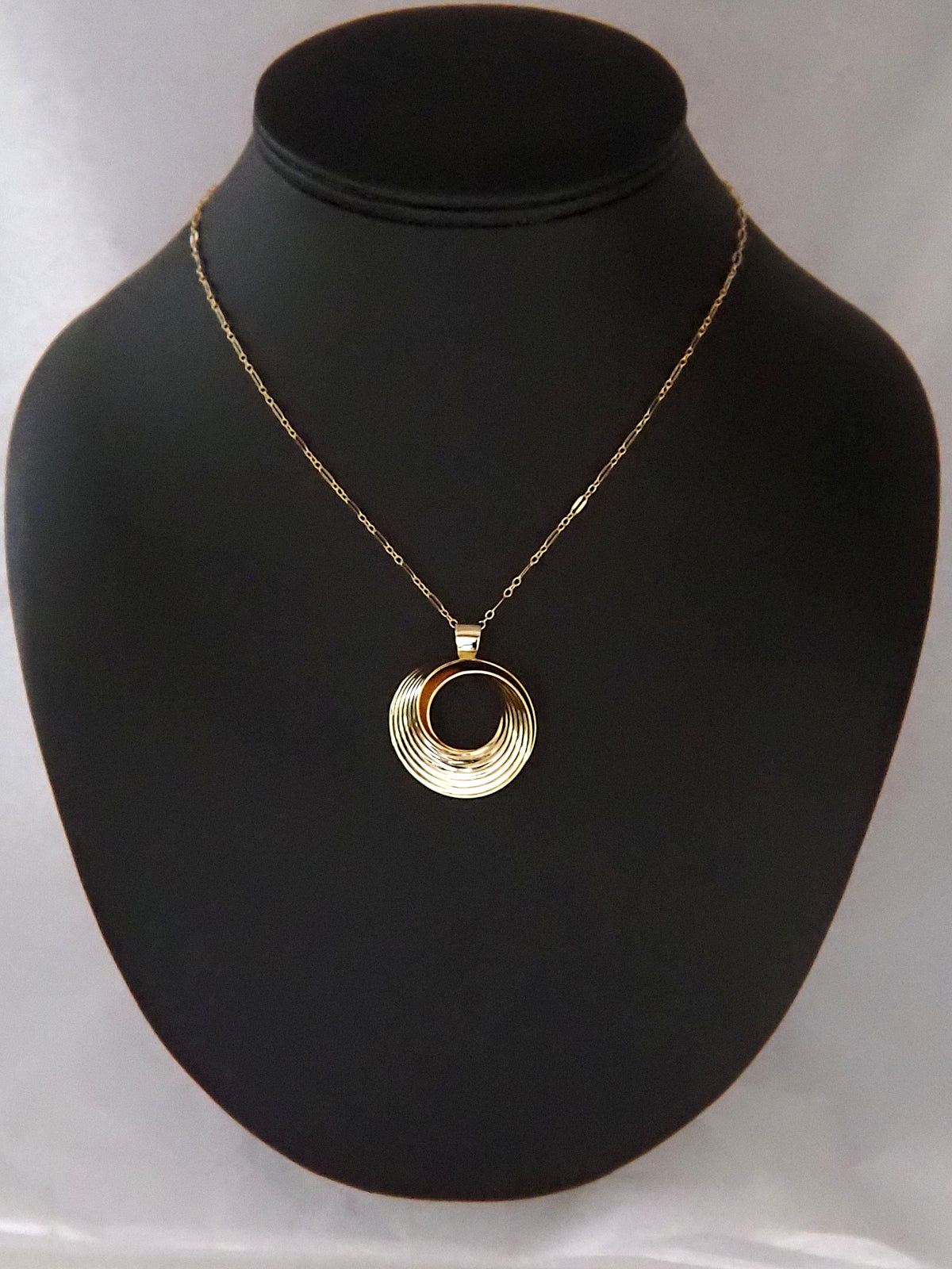 Photograph of a round, gold-plated silver pendant in the shape of a Moebius strip split into two layers, and ridged on the outside, on a gold long-and-short loop chain.