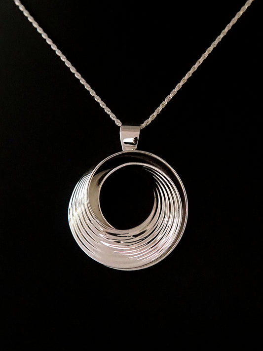 Photograph of a round, polished sterling silver pendant in the shape of a Moebius strip split into two layers, and ridged on the outside, on a sterling silver rope chain.