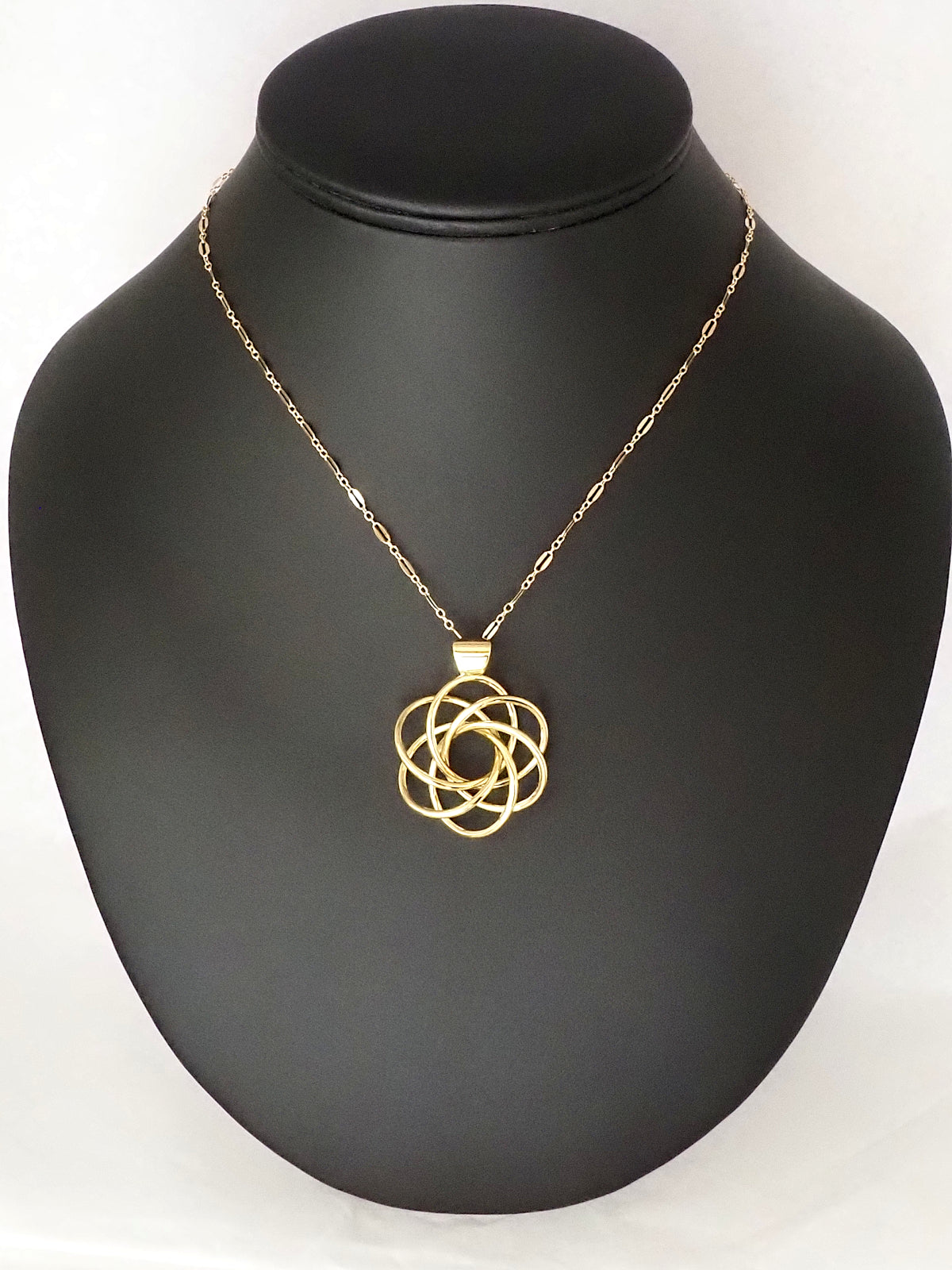 A  gold-plated brass pendant in an abstract shape resembling a flower with six petals, with a gold-filled loop chain, on a necklace display.