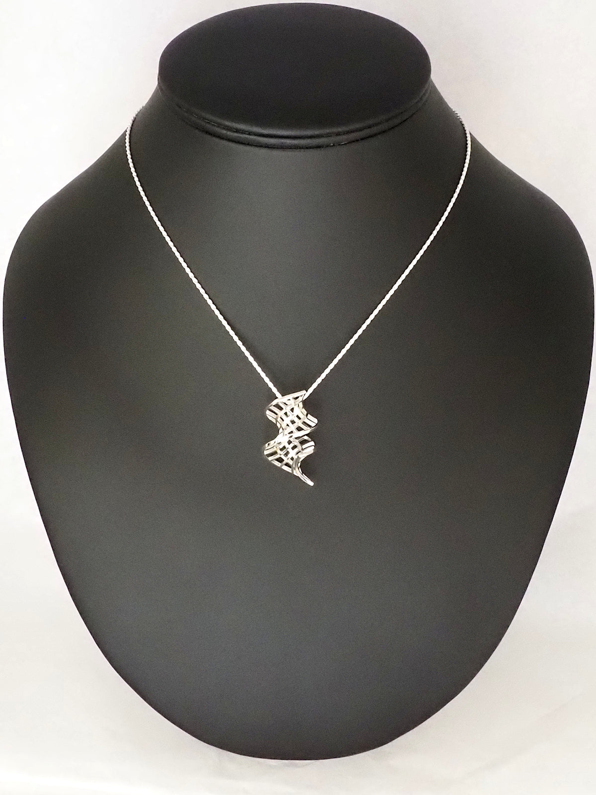 A silver catenoid-helicoid pendant with a silver French rope chain on a necklace display.
